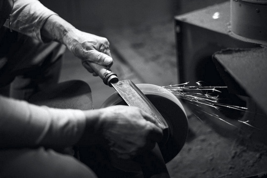 black and white photo of a man sharpening a kitchen knife on a grinding stone